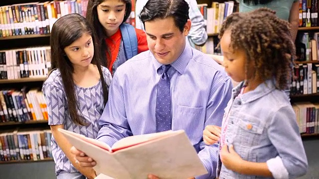 教师、图书管理员在图书馆或教室里为小学生读书。视频素材