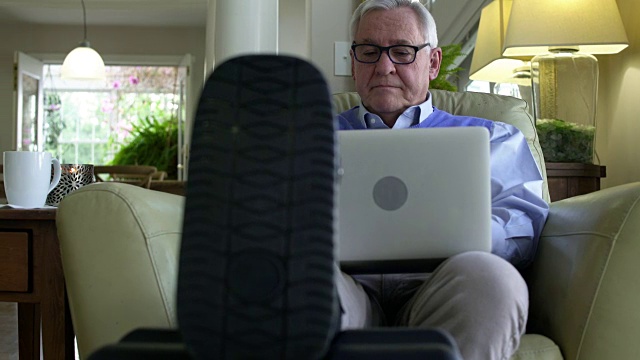 一个老人在家里用笔记本电脑支撑着他断了的腿视频素材
