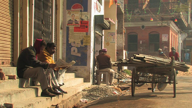 印度北方邦瓦拉纳西，两名男子在街上的台阶上看报纸视频下载