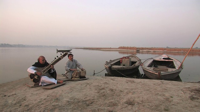 两名男子在印度北方邦瓦拉纳西恒河岸边演奏锡塔琴和邦戈鼓视频素材
