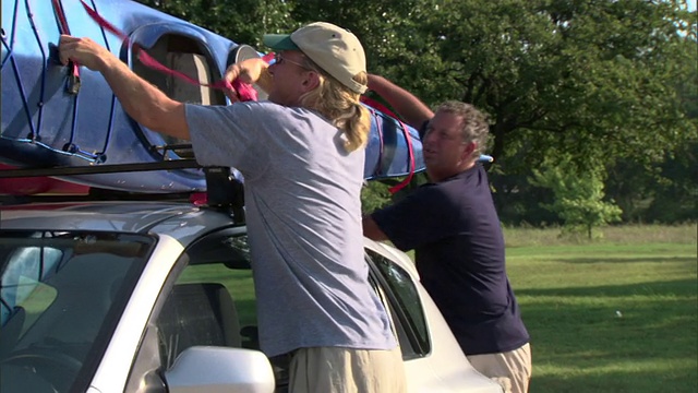 两名成年男子从车顶架上解开皮艇/美国德克萨斯州视频素材