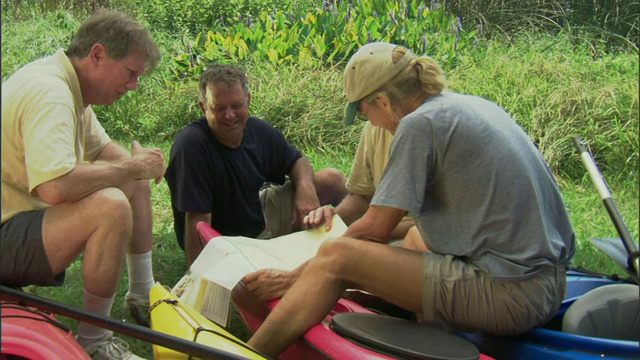 四名男子坐在皮划艇旁看地图/美国德克萨斯州达拉斯的白石湖视频素材