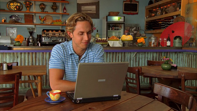 美国加州摩洛湾，一名年轻人在咖啡店使用笔记本电脑视频素材