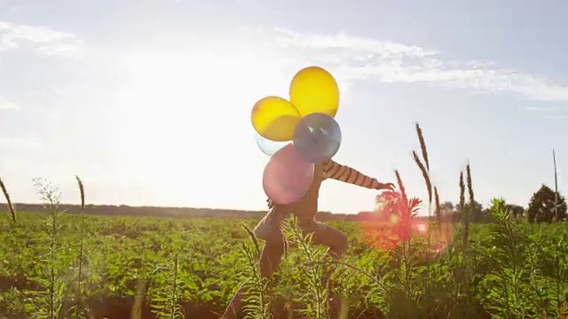 慢跑和奔跑的小女孩与气球在绿色的田野在日落视频素材