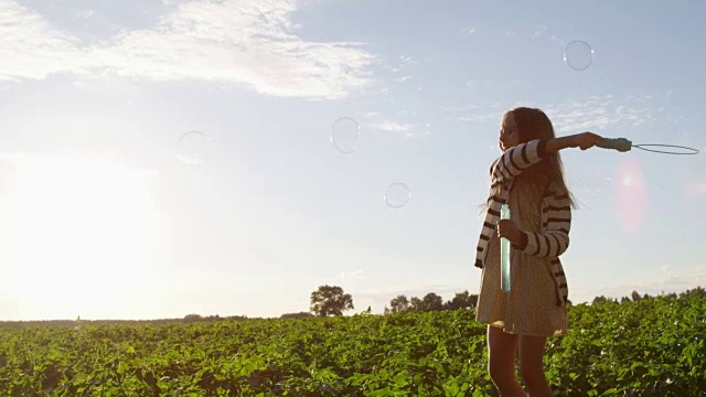 玩小女孩与空气泡泡在田野上在夏天在日落视频素材