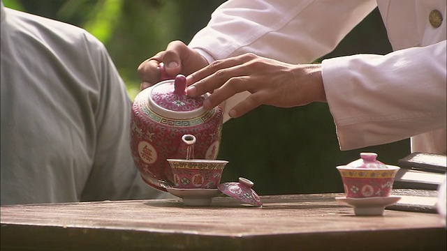 CU, PAN，男子倒茶到两个装饰杯，手特写，新加坡视频素材