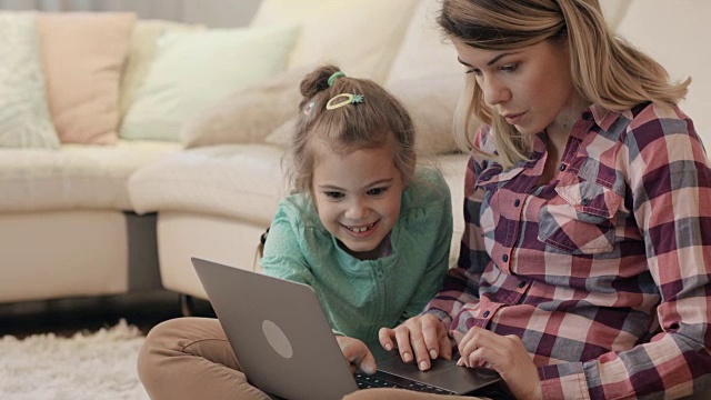 年轻的母亲在家里用笔记本电脑和她的女儿。视频素材