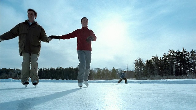 (远景)两个男孩在结冰的池塘上打曲棍球/一对夫妇手拉着手滑冰/缅因州视频下载