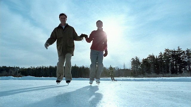 在背景/缅因州，一对手牵着手在结冰的池塘上滑冰的夫妇视频下载