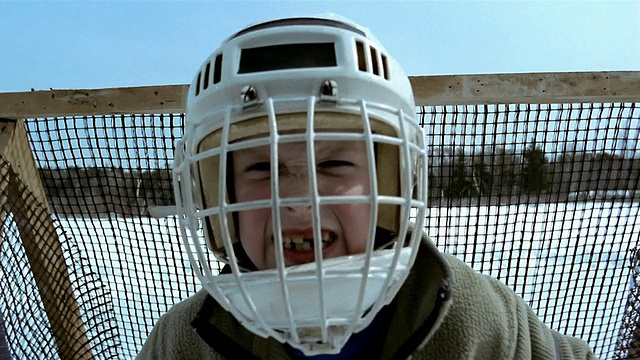 拉近镜头，小男孩戴着守门员面具，站在冰球门前/做鬼脸视频下载