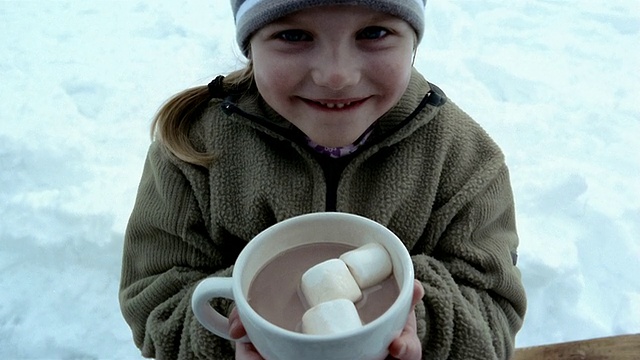 高角度特写倾斜下年轻的女孩喝着一杯热巧克力和棉花糖/微笑着在CAM视频下载