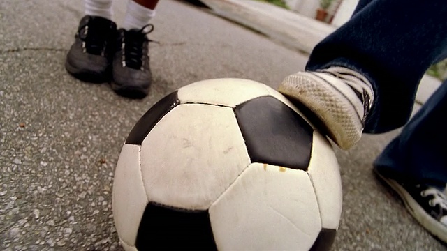 高角度近距离跟踪射门足球滚过街道/被孩子的脚停止和踢视频下载
