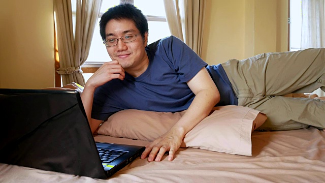 快乐的男人戴着眼镜用笔记本电脑在床上聊天聊天-家庭室内场景视频素材