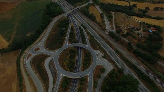 无人机在高速公路上空拍摄的航拍画面，这是加泰罗尼亚地区的工业区，高速公路上有环形车道，火车在同一方向行驶。4 k UHD。视频下载