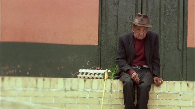 哥伦比亚波哥大，一名老妇人戴着软呢帽，拄着手杖坐在窗台上视频下载