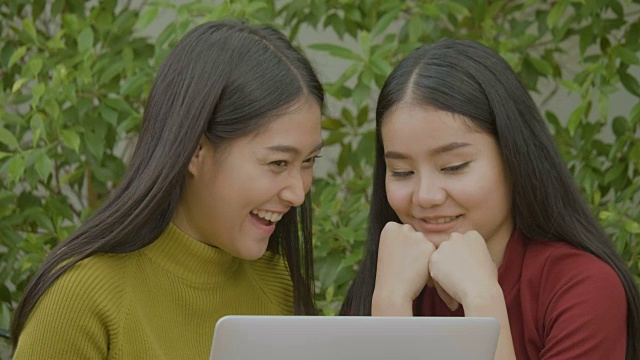 两个兴奋的亚洲漂亮女孩使用笔记本电脑，网上购物出售视频素材