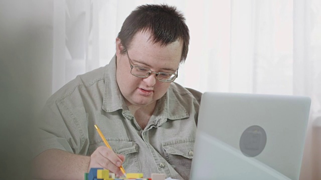 微笑的唐氏综合症患者使用笔记本电脑在家工作视频下载