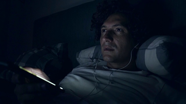英俊的男人在床上听音乐。视频素材
