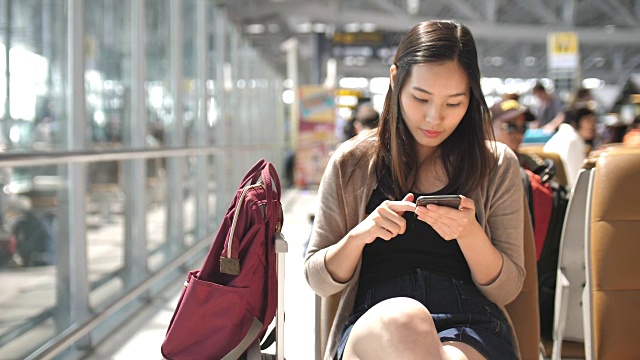 亚洲年轻女子在等待航班时触摸智能手机，慢镜头视频素材