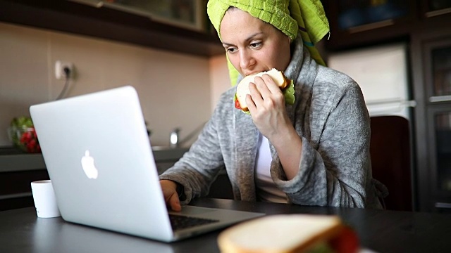 微笑的年轻女子使用笔记本电脑在厨房在家视频下载