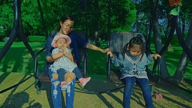 年轻的母亲和两个女儿在公园的摇椅上享受大自然视频素材