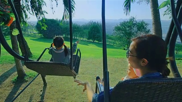 年轻的母亲和两个女儿在公园的摇椅上享受大自然视频素材