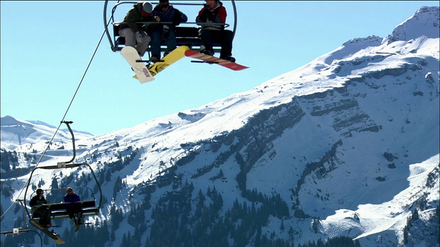 中镜头滑雪板驾驶滑雪缆车与雪山在背景/扔雪球的其他车手视频购买