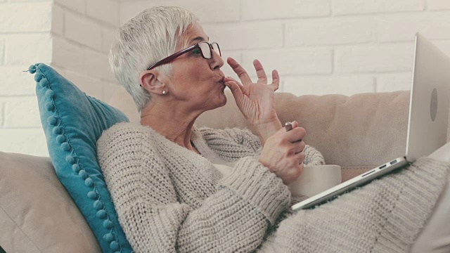 快乐成熟的女人，一边坐在沙发上吃麦片，一边用笔记本电脑视频聊天。视频素材