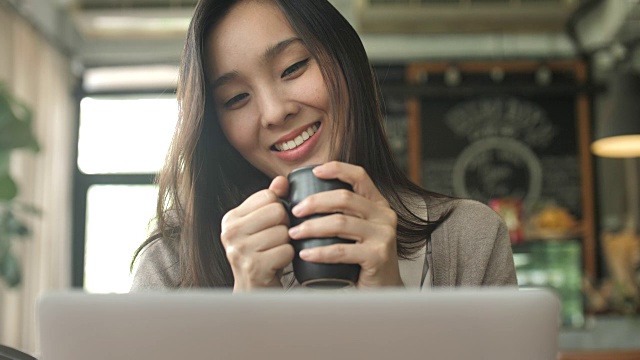 年轻女子看着笔记本电脑屏幕上的咖啡杯，慢动作视频下载
