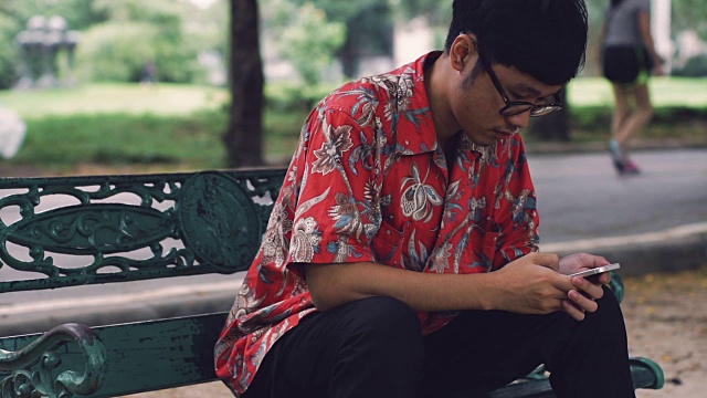 一名亚洲男子在公园内使用手机的画面。视频素材