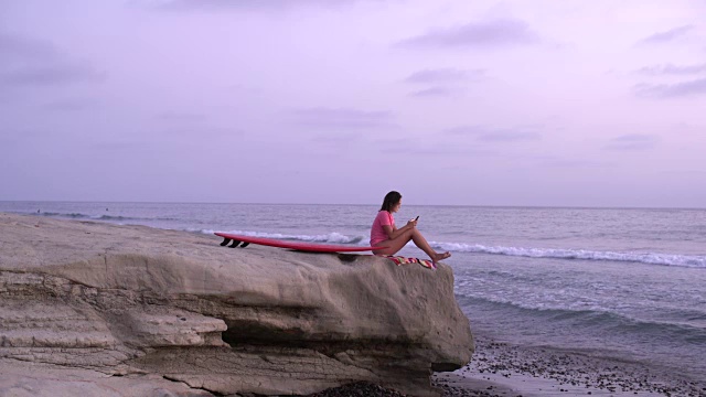 一名年轻女子冲浪后坐在一块岩石上视频下载