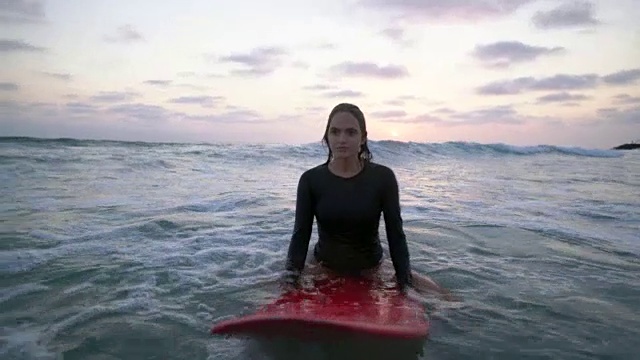 一个年轻女子坐在水里的冲浪板上视频下载