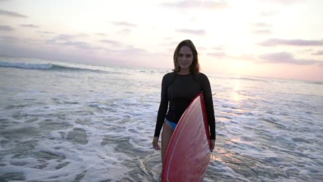 一个年轻女子在海滩上拿着一块红色的冲浪板视频下载