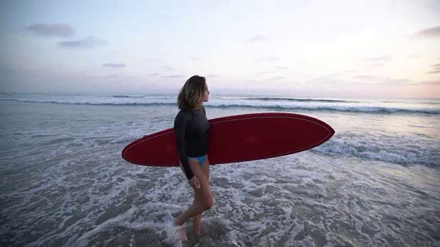 一个年轻女子拿着冲浪板沿着海滩走视频下载