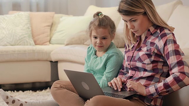 年轻的母亲和她的小女儿在客厅里使用笔记本电脑聊天。视频素材