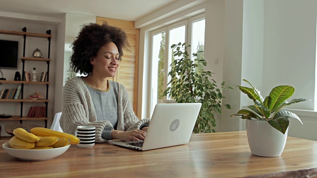 快乐的非裔美国女人一边喝咖啡一边在笔记本电脑上写电子邮件。视频素材