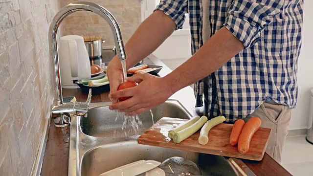 一个面目全非的男人在厨房做饭时洗菜。视频素材