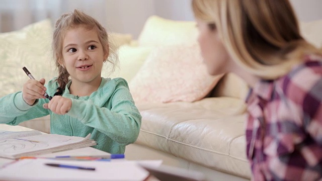 可爱的小女孩一边在纸上画画，一边和妈妈说话。视频素材