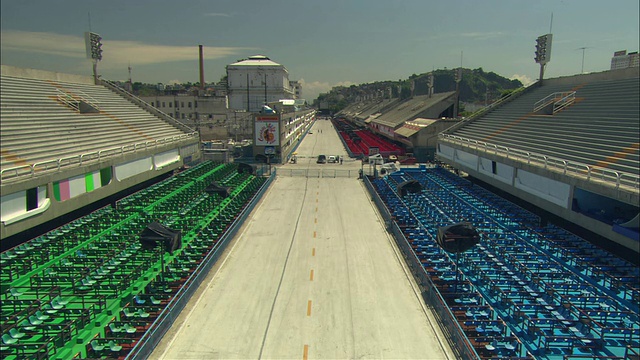 明亮的蓝色和绿色的座位在跑道对面的运动区域，人们在远处准备赛事/巴西视频下载