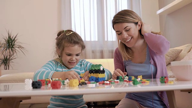 快乐的母亲和女儿玩的时候，在家里玩拼图。视频素材