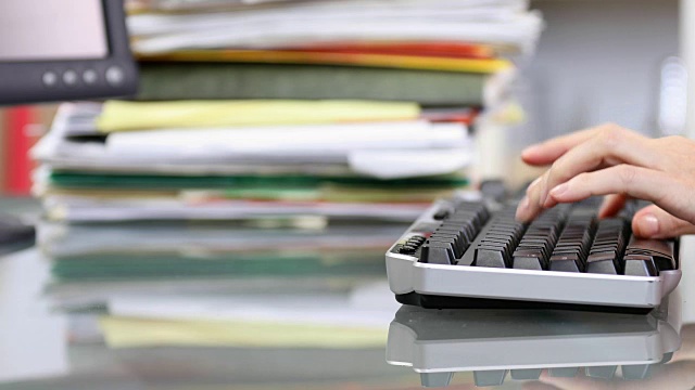 办公室职员在电脑键盘上打字，堆放文件。视频下载
