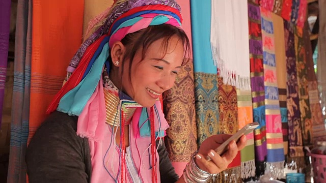 一名妇女穿着传统服装，拿着手机在村里织布视频下载