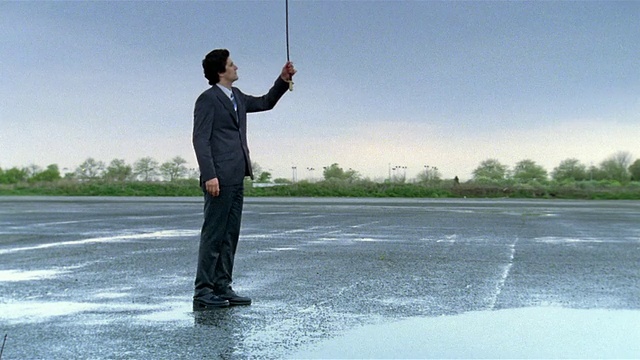 宽镜头商人拉着挂在天空的链子在空的停车场/让它下雨/让雨停止视频下载