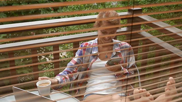微笑的女人在阳台上放松，用智能手机发短信视频素材