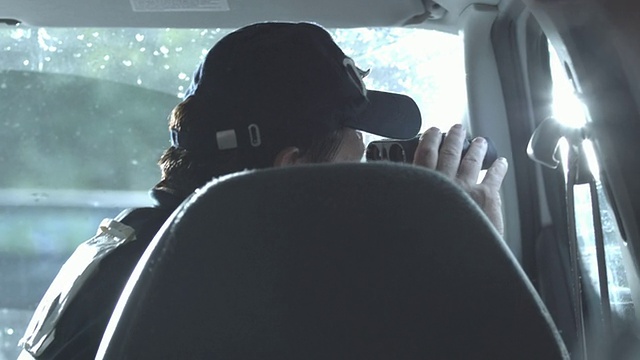 美国纽约州，斯塔顿岛，一名警察坐在警车里用望远镜观察视频下载
