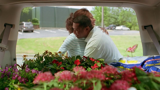 在花园中心的停车场，一对情侣在把植物装进SUV的后座后拥抱在一起视频素材