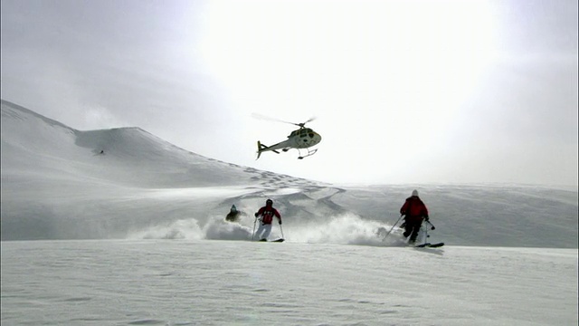 在加拿大不列颠哥伦比亚省的卡利布山和莫纳西山，直升飞机在五名滑雪者的上方滑行视频下载