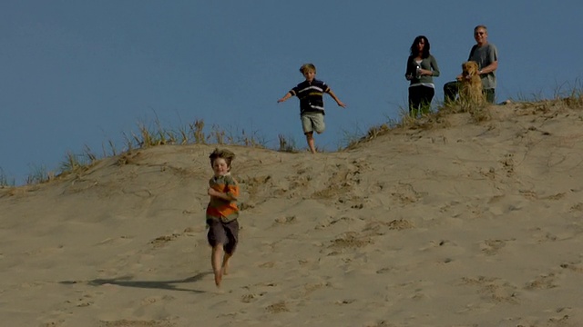 WS, CU，两个男孩(8-9,10-11)在沙丘上奔跑，父母在背景中，美国马萨诸塞州科德角普罗文斯敦视频素材