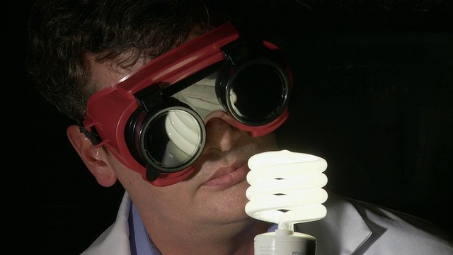科学家戴着护目镜打开并观察节能灯泡，亚特兰大，乔治亚州，美国视频下载