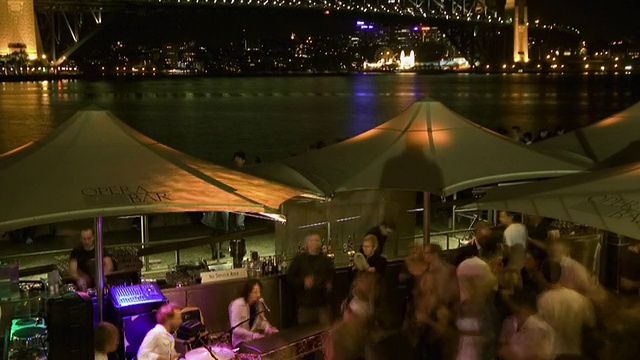 T/L, TD, MS，灯火通明的悉尼海港大桥和人们晚上在室外咖啡馆跳舞，悉尼，澳大利亚视频素材